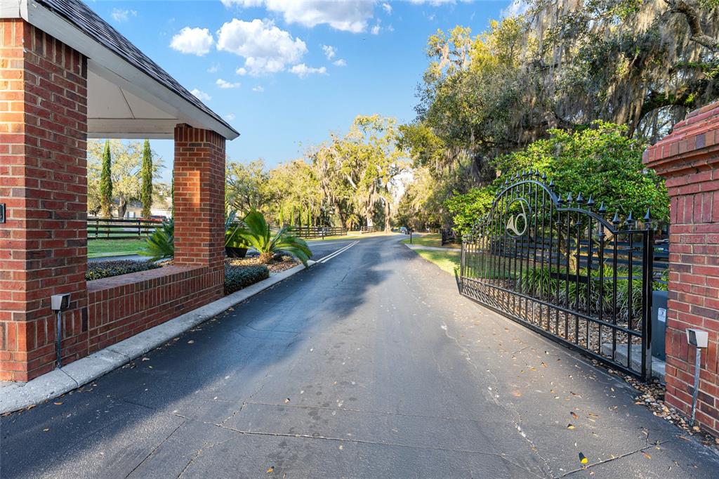 An asphalt driveway leads through a brick-pillared entrance with an open black metal gate — 14312 NW 41ST AVENUE, NEWBERRY, FL