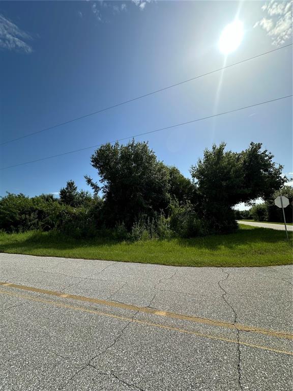 A paved road leads to a grassy lot with dense trees under a bright sun — 12088 HENLEY AVENUE, PORT CHARLOTTE, FL