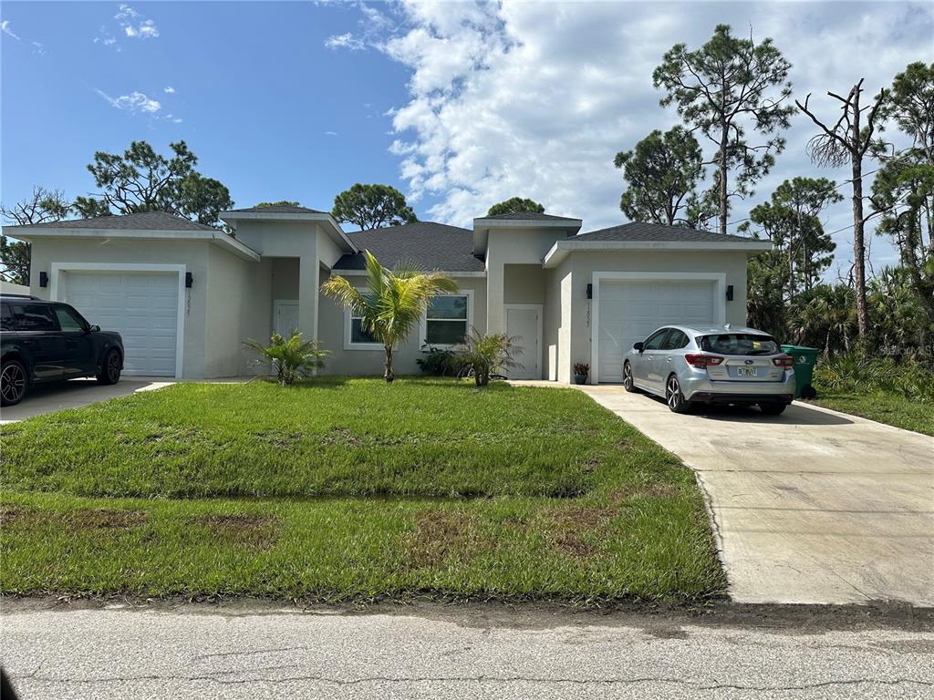 A single-story duplex with two garages, a grassy front yard, and two parked cars — 12088 HENLEY AVENUE, PORT CHARLOTTE, FL