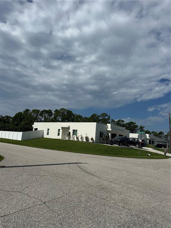 A modern, white, single-story house sits on a grassy corner lot under a cloudy sky — 12088 HENLEY AVENUE, PORT CHARLOTTE, FL