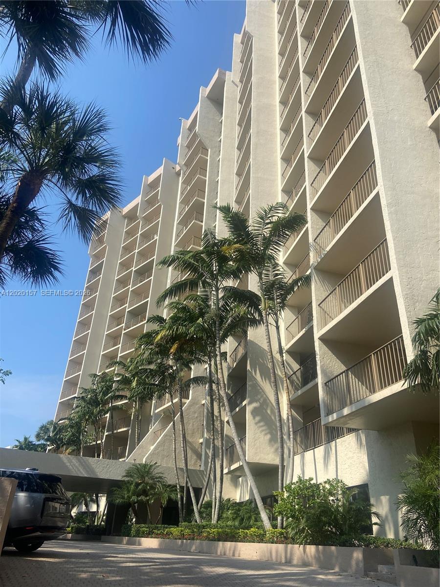 A low-angle view of a tall, multi-story residential building with balconies and surrounding palm trees — LAUDERDALE BY THE SEA, FL