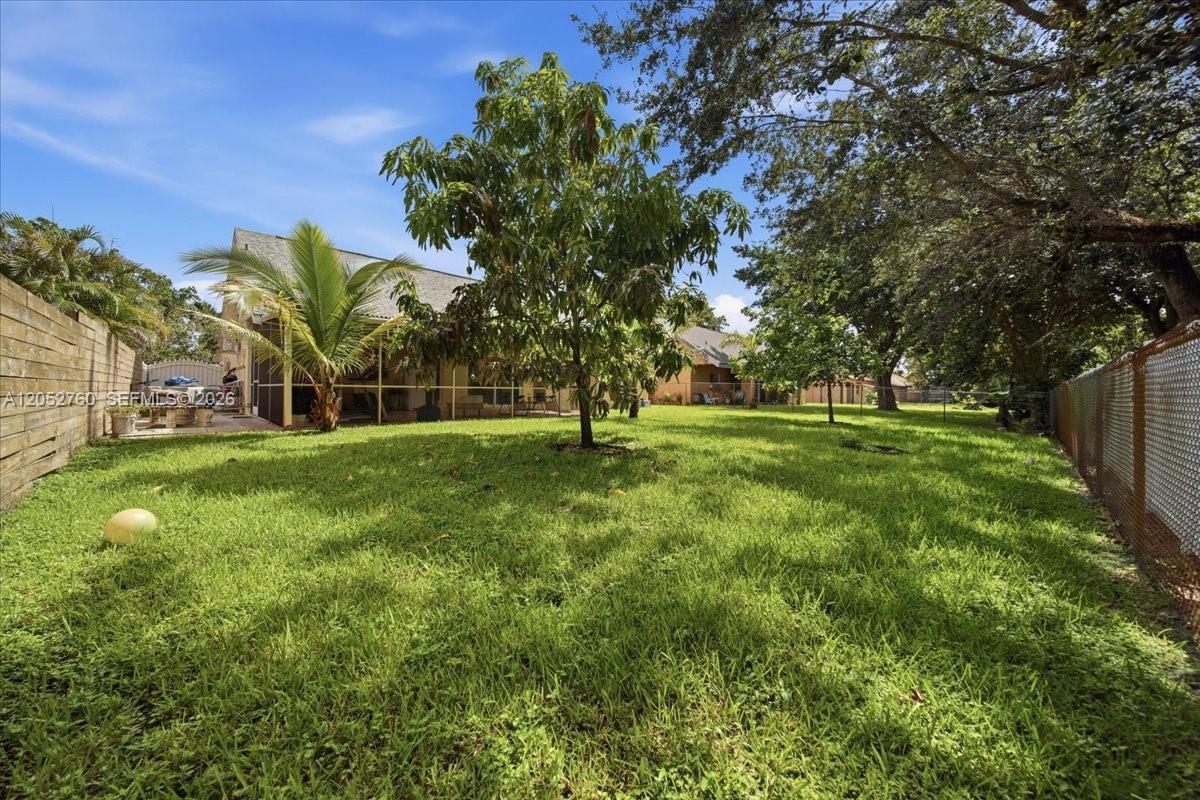 A grassy backyard features a screened-in patio, several trees, and a chain-link fence — 9050 Crescent Dr, Miramar FL 33025, MIRAMAR, FL