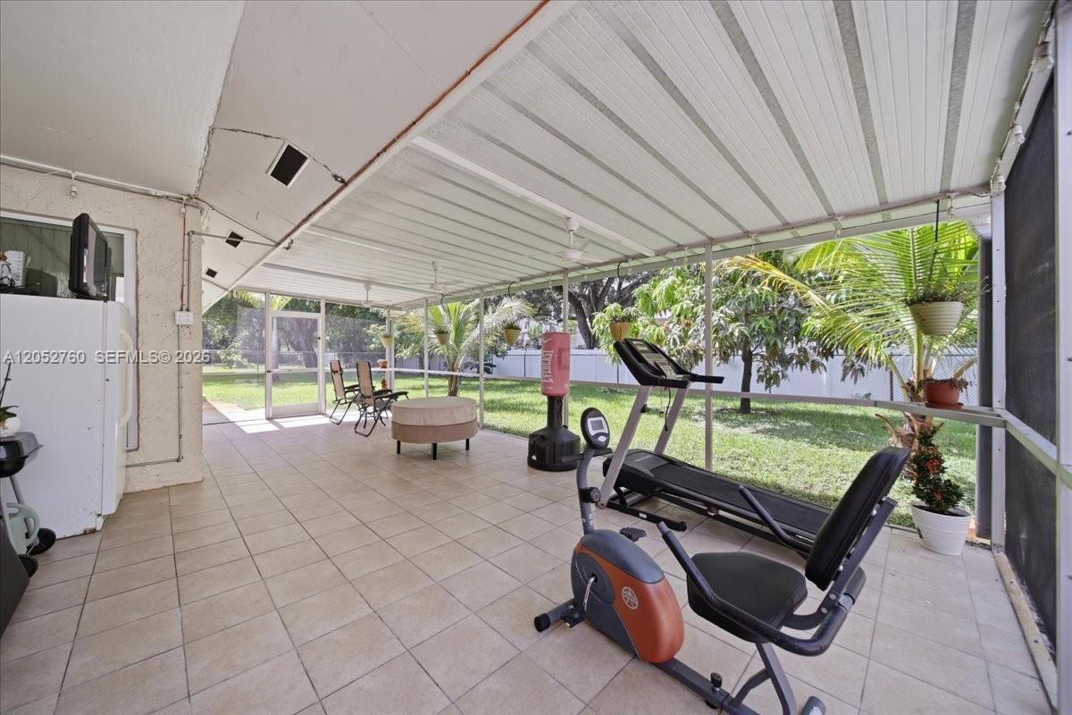 A tiled, screened-in patio features a treadmill, exercise bike, and a view of the yard — 9050 Crescent Dr, Miramar FL 33025, MIRAMAR, FL