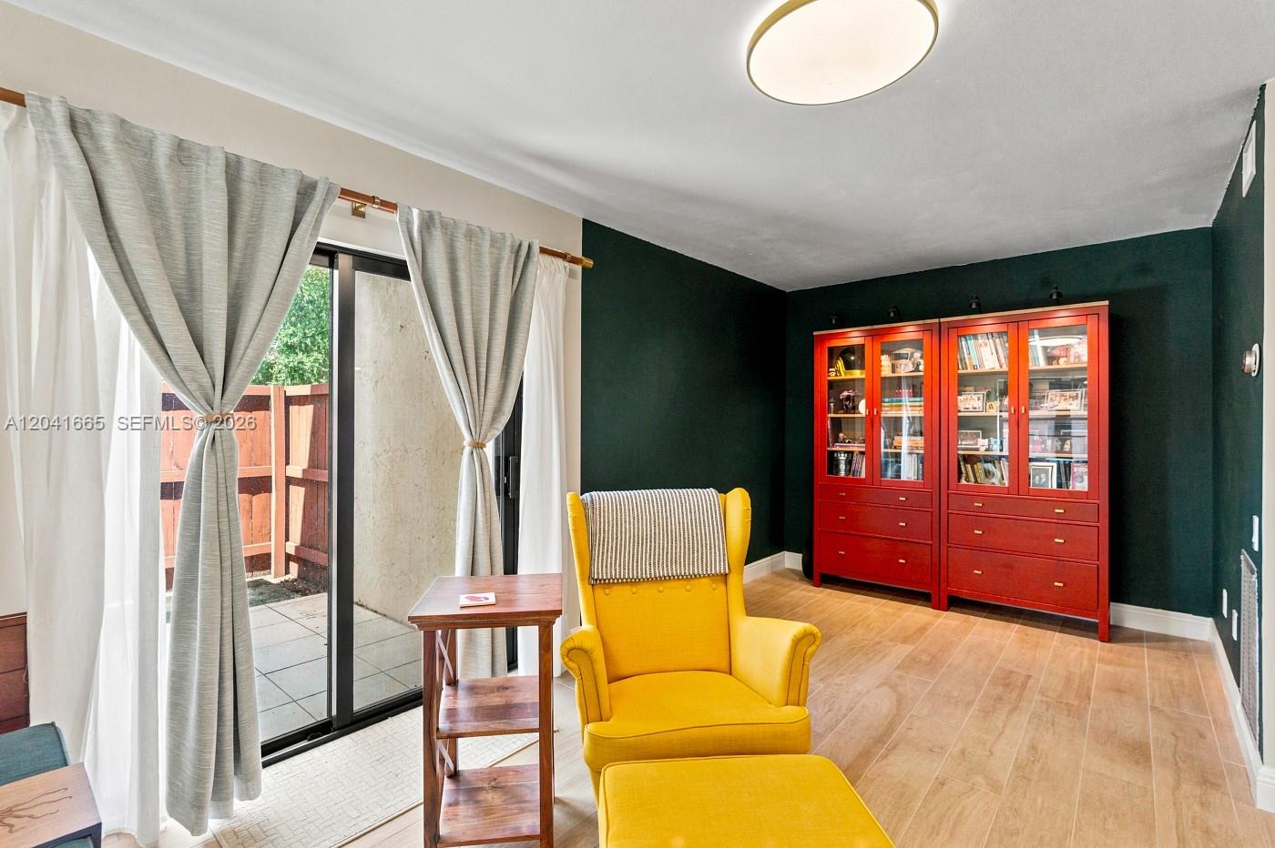 A room with dark green walls, wood-look flooring, a yellow armchair, and red bookshelves — 6231 SW 116th Pl # G, Miami FL 33173, MIAMI, FL