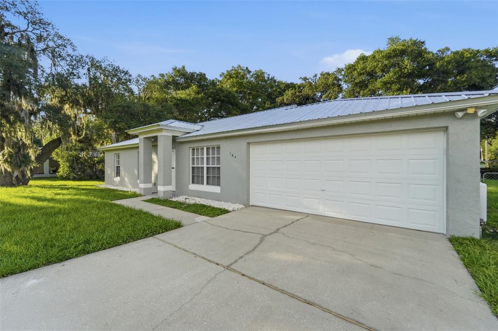 A single-story house with a white metal roof, gray stucco exterior, and a two-car garage — 164 DEBARY DRIVE, DEBARY, FL