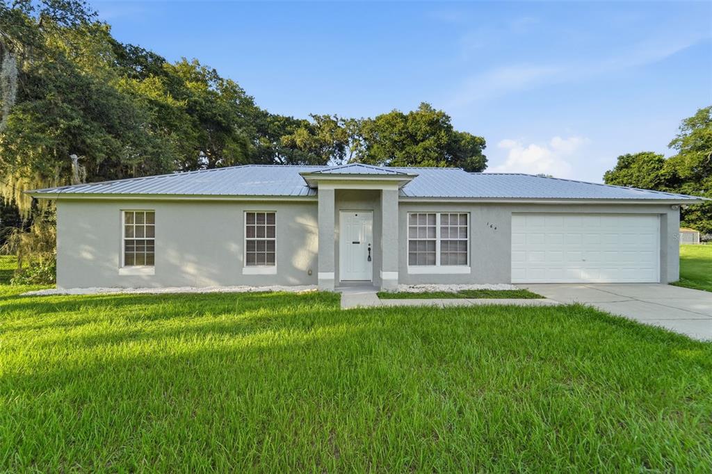 A single-story house with a gray stucco exterior, a metal roof, and a white garage door — 164 DEBARY DRIVE, DEBARY, FL