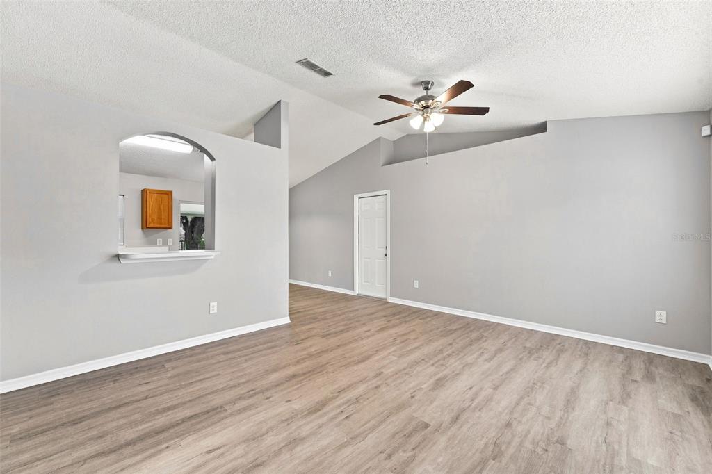 A living room with light gray walls, wood-look flooring, a vaulted ceiling, and a pass-through window — 164 DEBARY DRIVE, DEBARY, FL