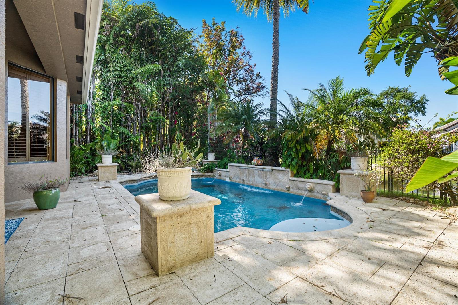 A backyard patio features a small swimming pool with a stone fountain and tropical landscaping — 3483 Collonade Drive, Wellington FL 33449, WELLINGTON, FL