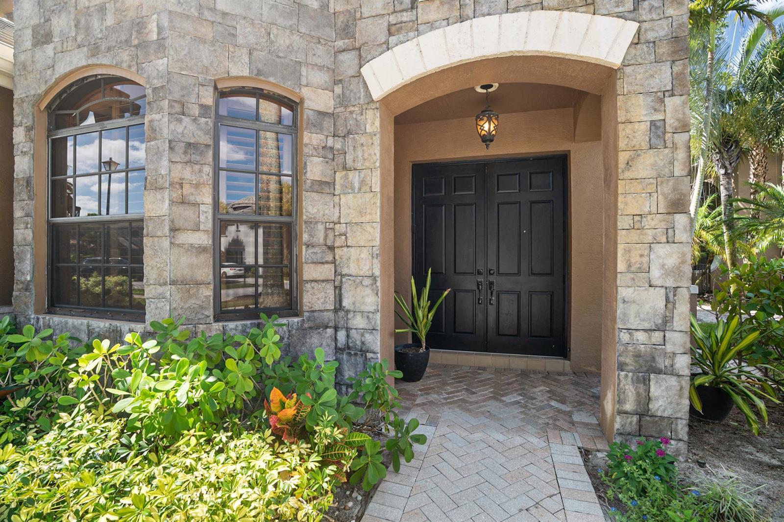 A stone-faced house exterior features a double front door, arched windows, and a brick walkway — 3483 Collonade Drive, Wellington FL 33449, WELLINGTON, FL