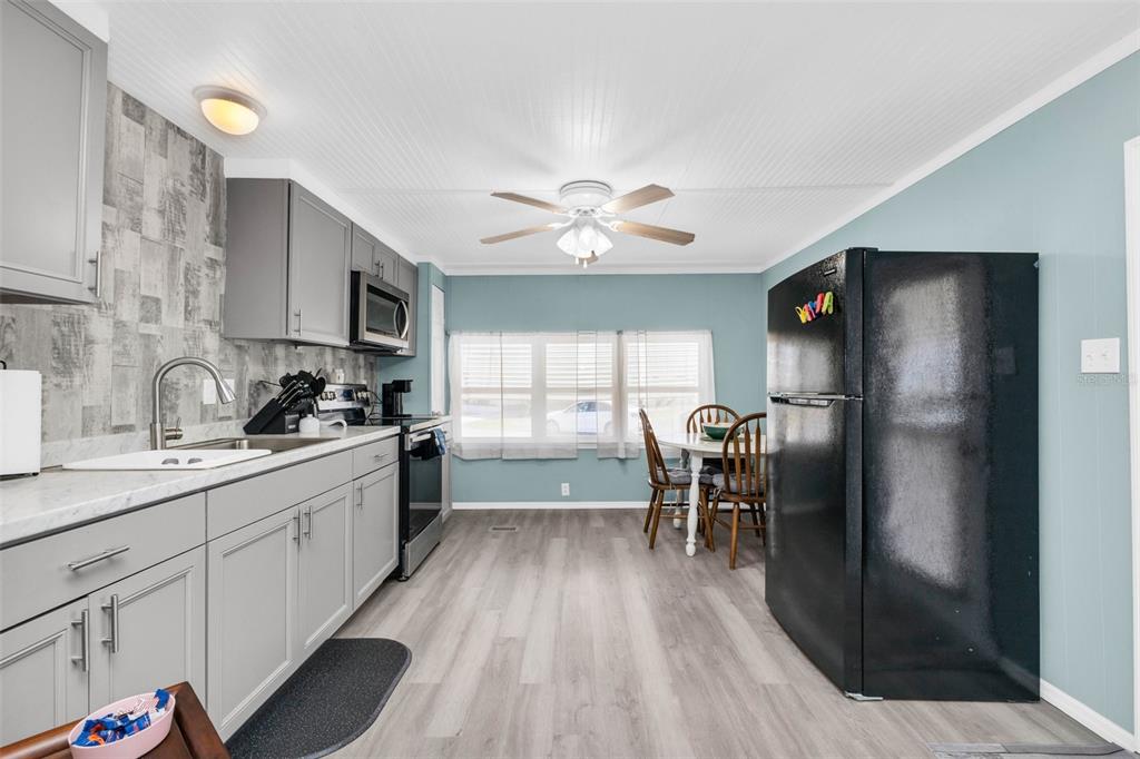 A kitchen with gray cabinets, a black refrigerator, and a dining table by a window — 6835 ANAPA COURT, NORTH PORT, FL