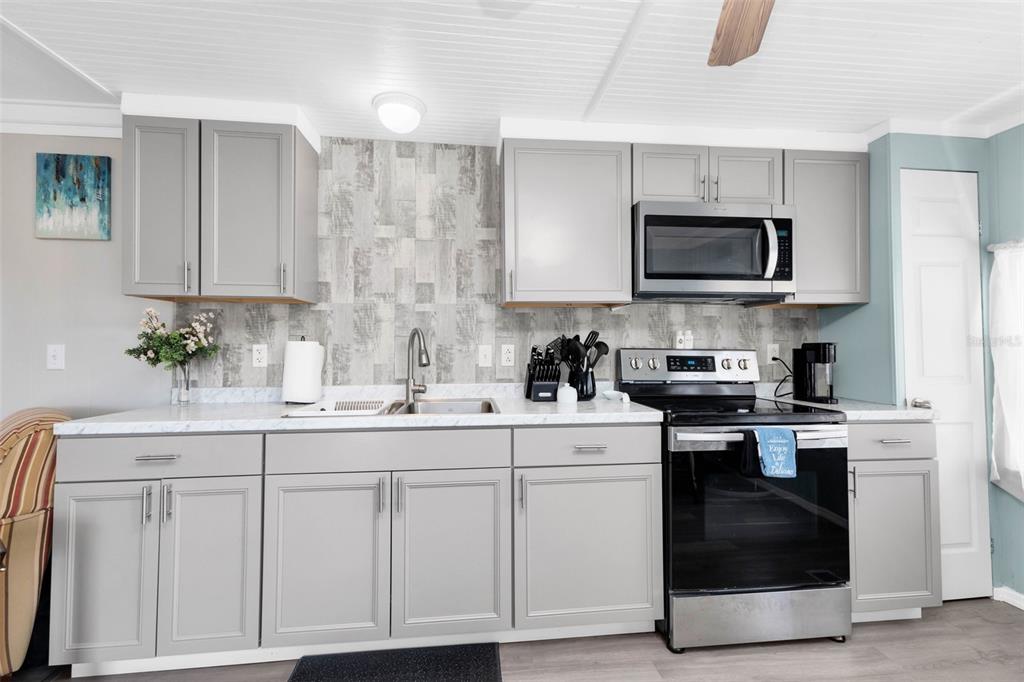 A kitchen features grey cabinets, a marble-look countertop, a tiled backsplash, and stainless steel appliances — 6835 ANAPA COURT, NORTH PORT, FL