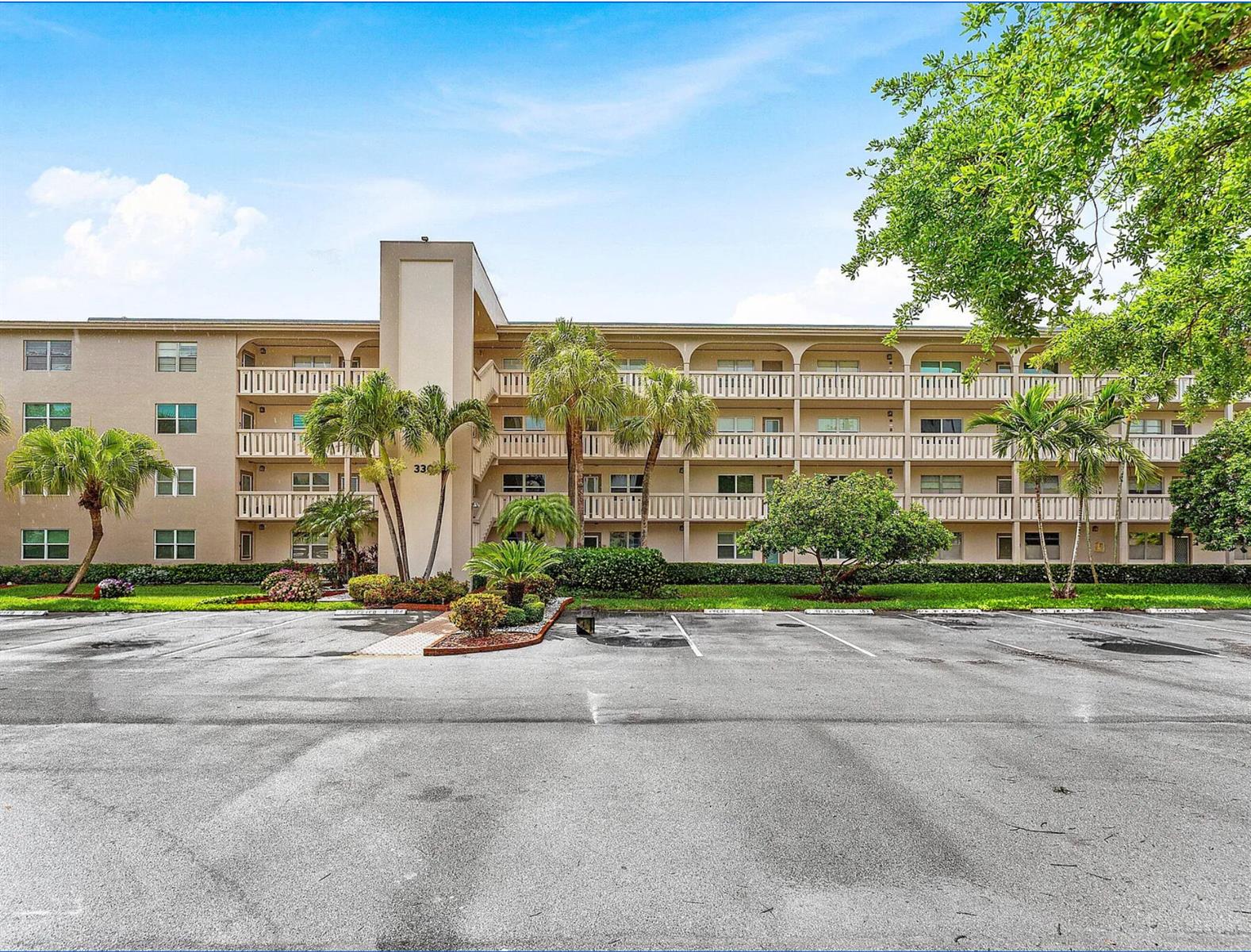A multi-story apartment building with balconies and palm trees sits behind a paved parking lot — 3301 Aruba Way # D3, Coconut Creek FL 33066, COCONUT CREEK, FL