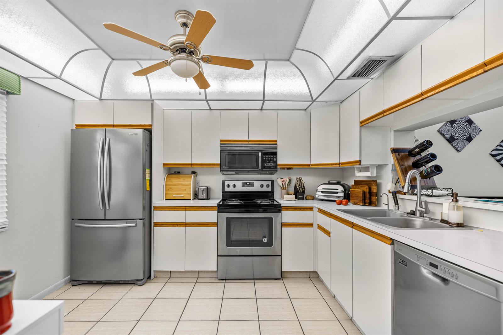 A kitchen features white cabinets with wood trim, stainless steel appliances, and a ceiling fan — 3301 Aruba Way # D3, Coconut Creek FL 33066, COCONUT CREEK, FL