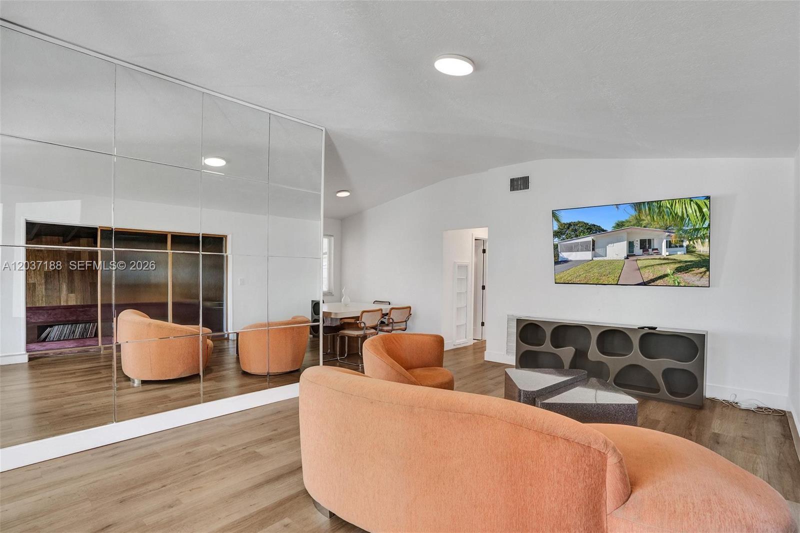 A living room features orange curved furniture, a mirrored wall, and a wall-mounted television — 581 NE 175th Ter, North Miami Beach FL 33162, NORTH MIAMI BEACH, FL