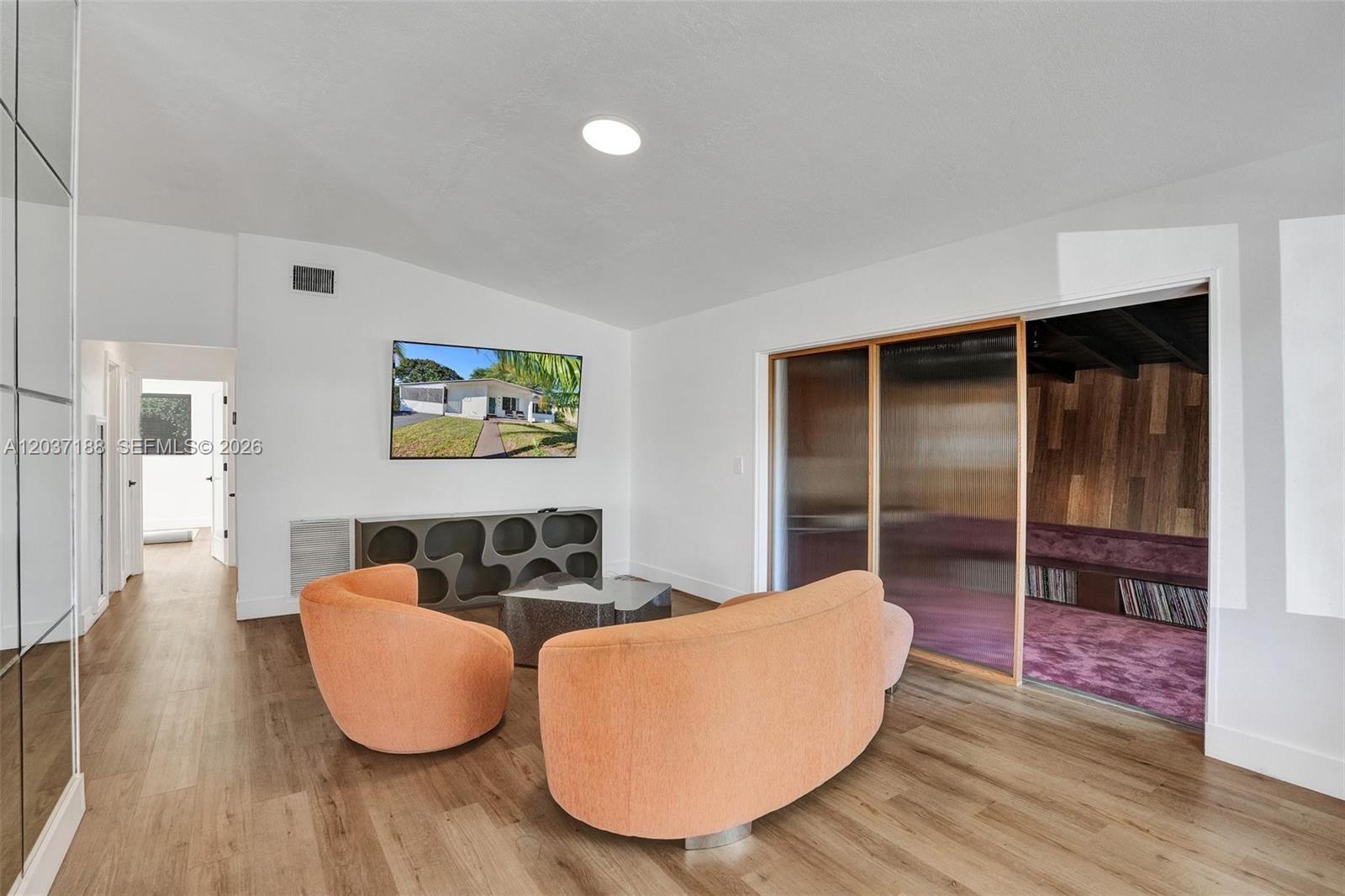A living room features orange curved seating, a media console, and a glass-enclosed room — 581 NE 175th Ter, North Miami Beach FL 33162, NORTH MIAMI BEACH, FL