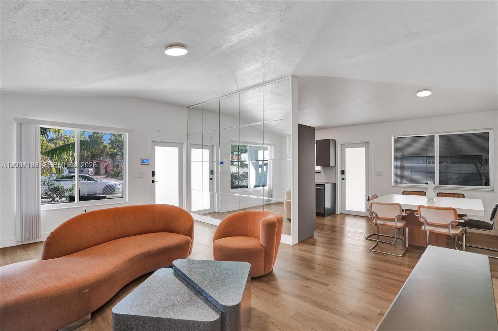 A living and dining area features orange furniture, mirrored walls, and light wood flooring — 581 NE 175th Ter, North Miami Beach FL 33162, NORTH MIAMI BEACH, FL