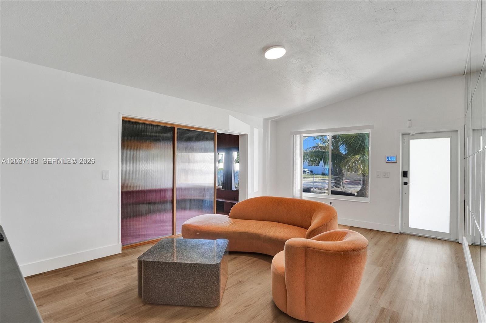 A living room features light wood flooring, an orange curved sofa, and a glass door — 581 NE 175th Ter, North Miami Beach FL 33162, NORTH MIAMI BEACH, FL