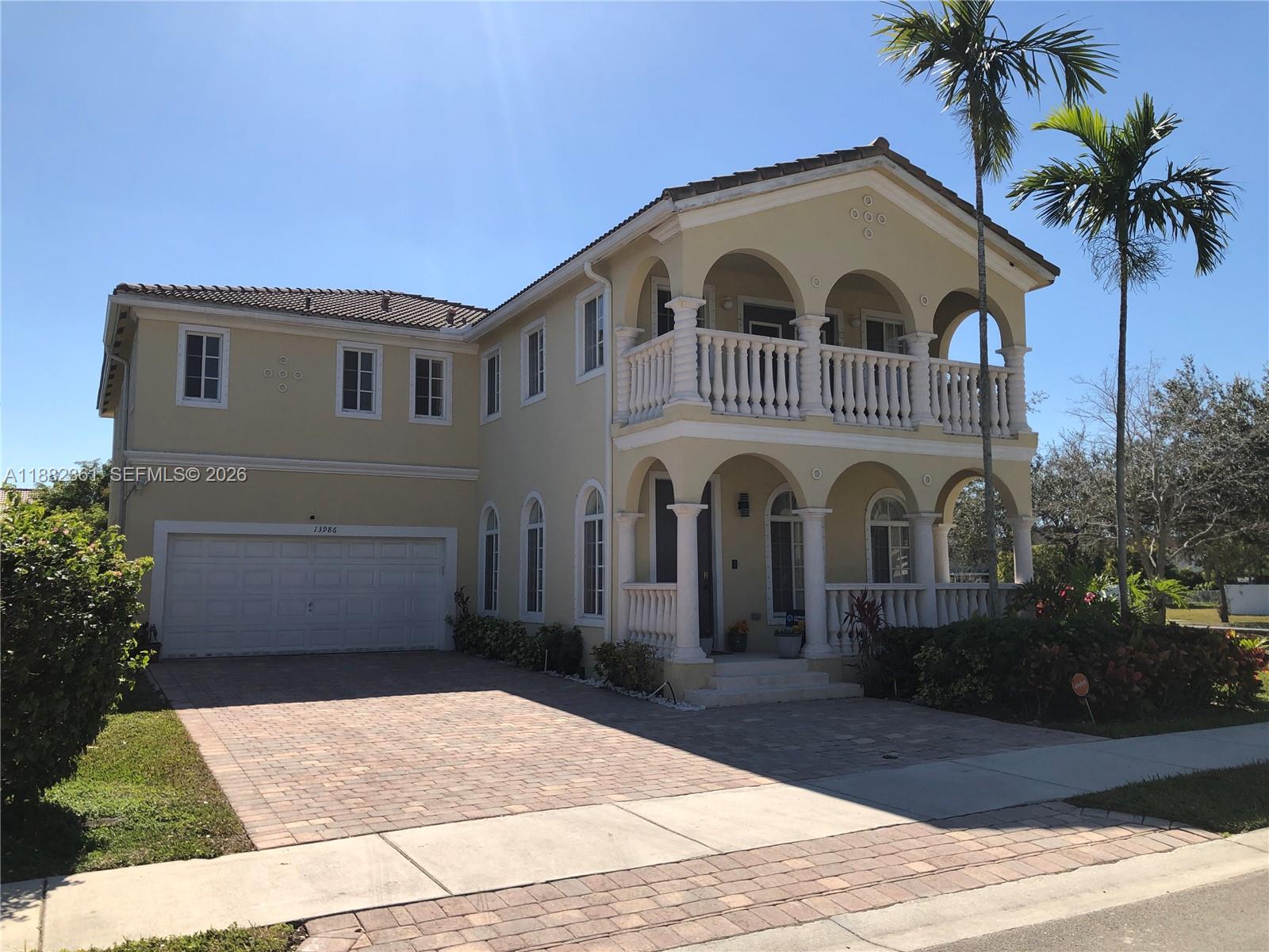 A two-story yellow house features a tiled roof, arched balconies, and a paved driveway — 13986 SW 276th Way, Homestead FL 33032, HOMESTEAD, FL