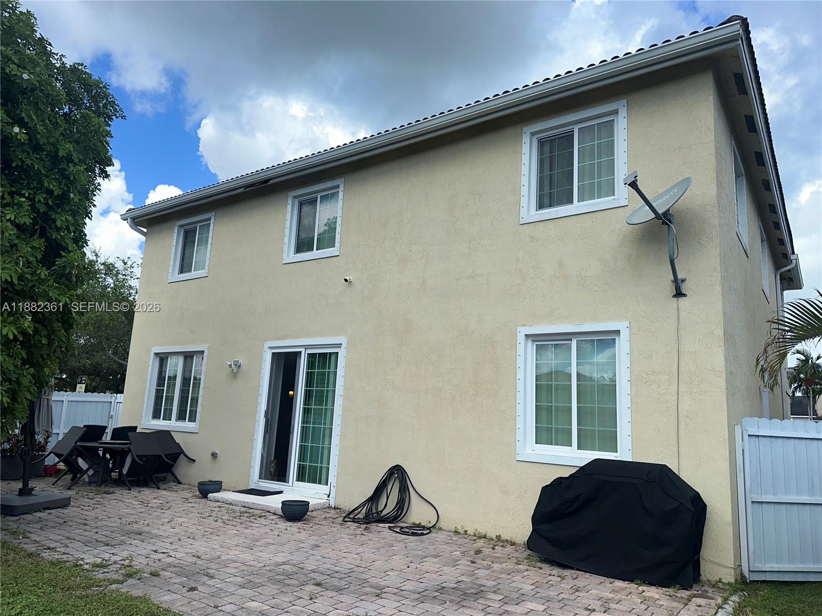 The exterior of a two-story beige house features a patio, sliding glass doors, and windows — 13986 SW 276th Way, Homestead FL 33032, HOMESTEAD, FL