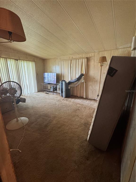 A living room with wood-paneled walls, brown carpeting, a portable air conditioner, and a mattress — 2642 MCDANIEL DRIVE, KISSIMMEE, FL