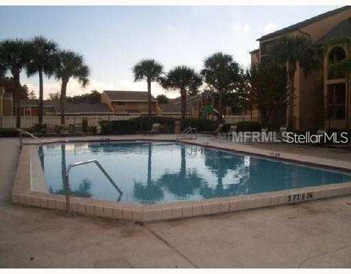 A rectangular swimming pool with depth markers is surrounded by a concrete deck and palm trees — 2031 CASCADES BOULEVARD UNIT 103, KISSIMMEE, FL
