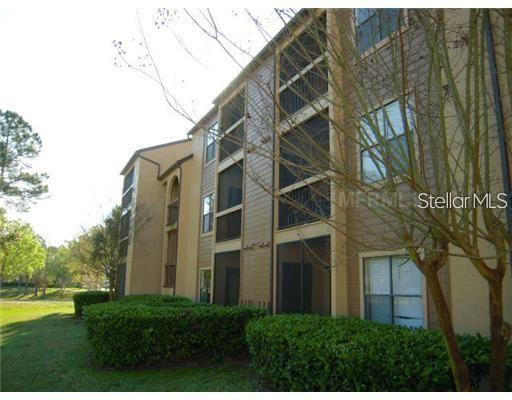 A three-story apartment building exterior features tan siding, screened balconies, and manicured green hedges — 2031 CASCADES BOULEVARD UNIT 103, KISSIMMEE, FL