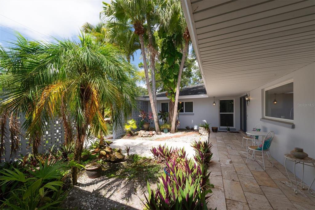 A paved patio area features tropical landscaping, palm trees, and a covered walkway with seating — 1350 FAIRWAY DRIVE, DUNEDIN, FL