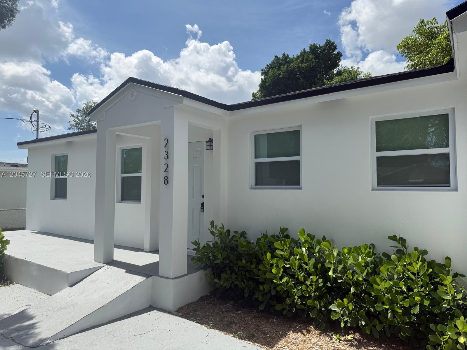 A white single-story house features a covered entryway, a concrete ramp, and green landscaping — 2328 NW 80th St, Miami FL 33147, MIAMI, FL