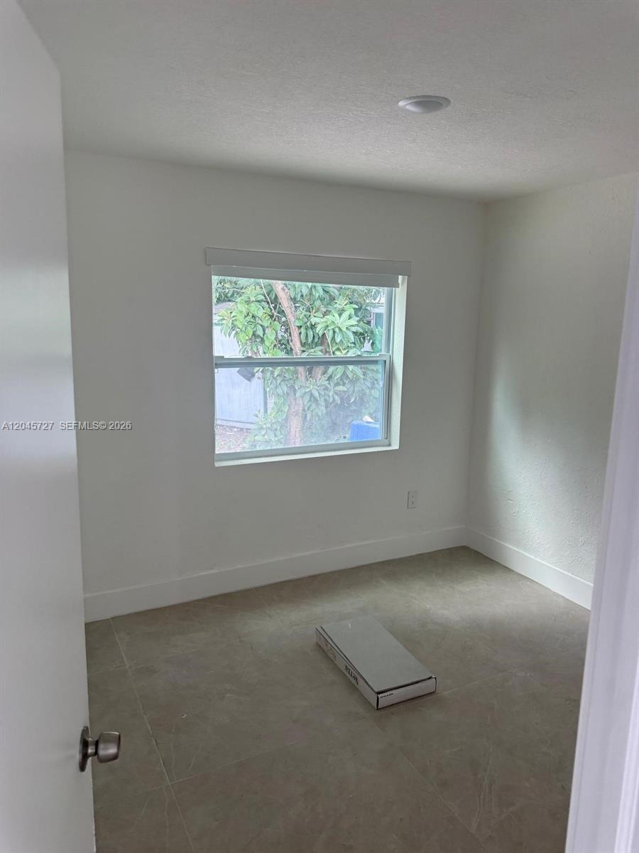 A small, empty room features white walls, light-colored tile flooring, and a single window — 2328 NW 80th St, Miami FL 33147, MIAMI, FL