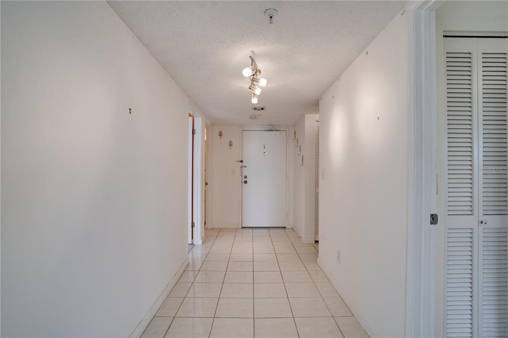 A hallway with white walls, tiled floors, and a ceiling-mounted light fixture leads to a door — 5940 PELICAN BAY PLAZA S UNIT 504, ST PETERSBURG, FL