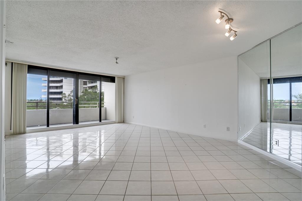 An empty living room features white tile flooring, a mirrored wall, and a sliding glass door — 5940 PELICAN BAY PLAZA S UNIT 504, ST PETERSBURG, FL