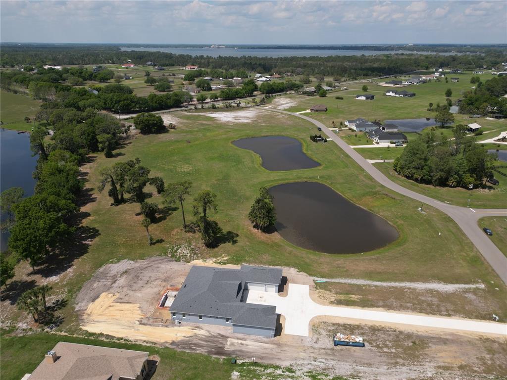An aerial view shows a newly constructed house with a concrete driveway near two ponds — 3430 LAKE DIANE ROAD, TAVARES, FL