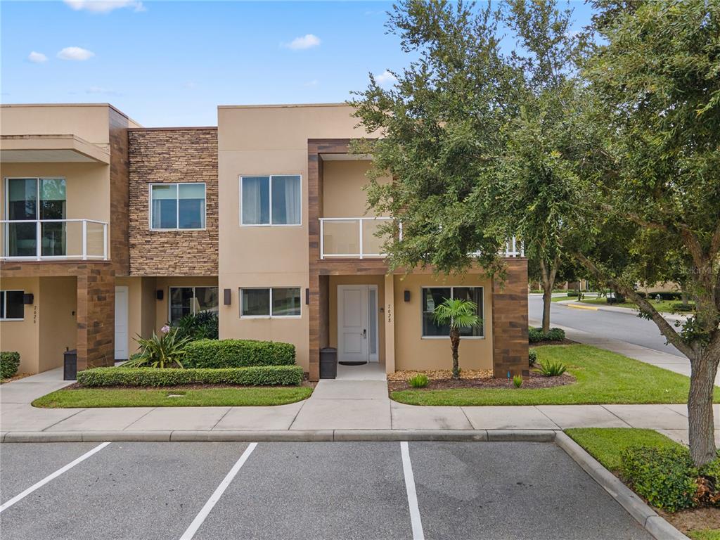 A two-story townhouse exterior features tan stucco, stone accents, and a small front balcony — 7628 RECIFE DRIVE, KISSIMMEE, FL