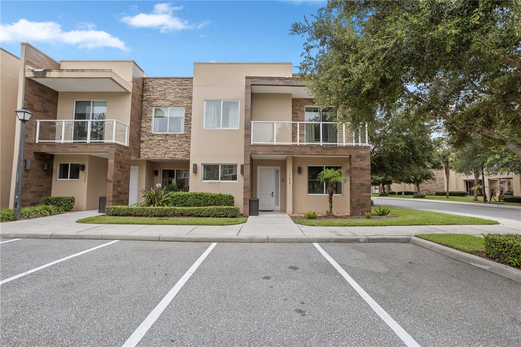 The exterior of a two-story townhouse features a stone facade, balconies, and a parking lot — 7628 RECIFE DRIVE, KISSIMMEE, FL