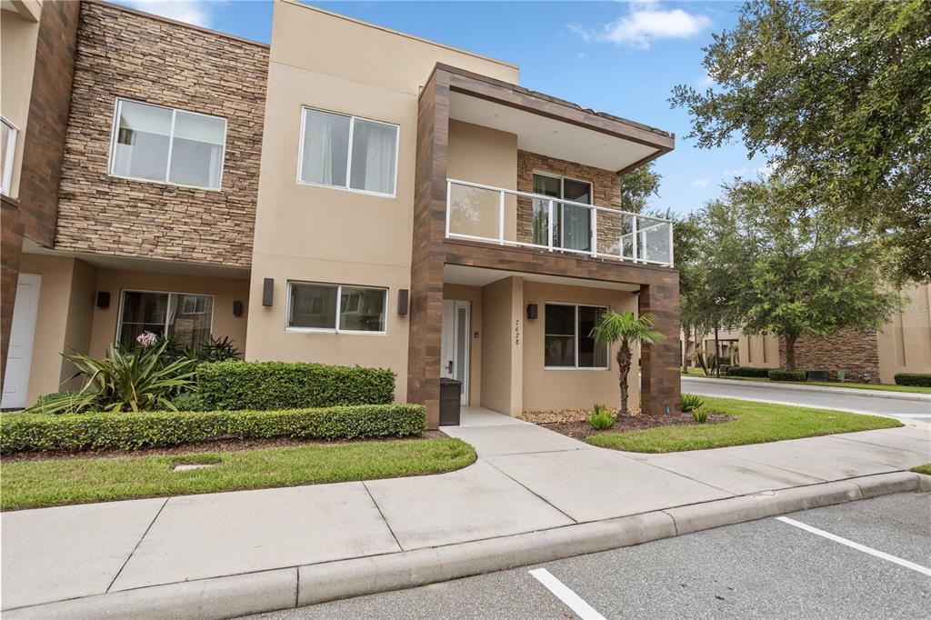A two-story townhouse exterior features tan stucco, stone accents, a balcony, and a front walkway — 7628 RECIFE DRIVE, KISSIMMEE, FL