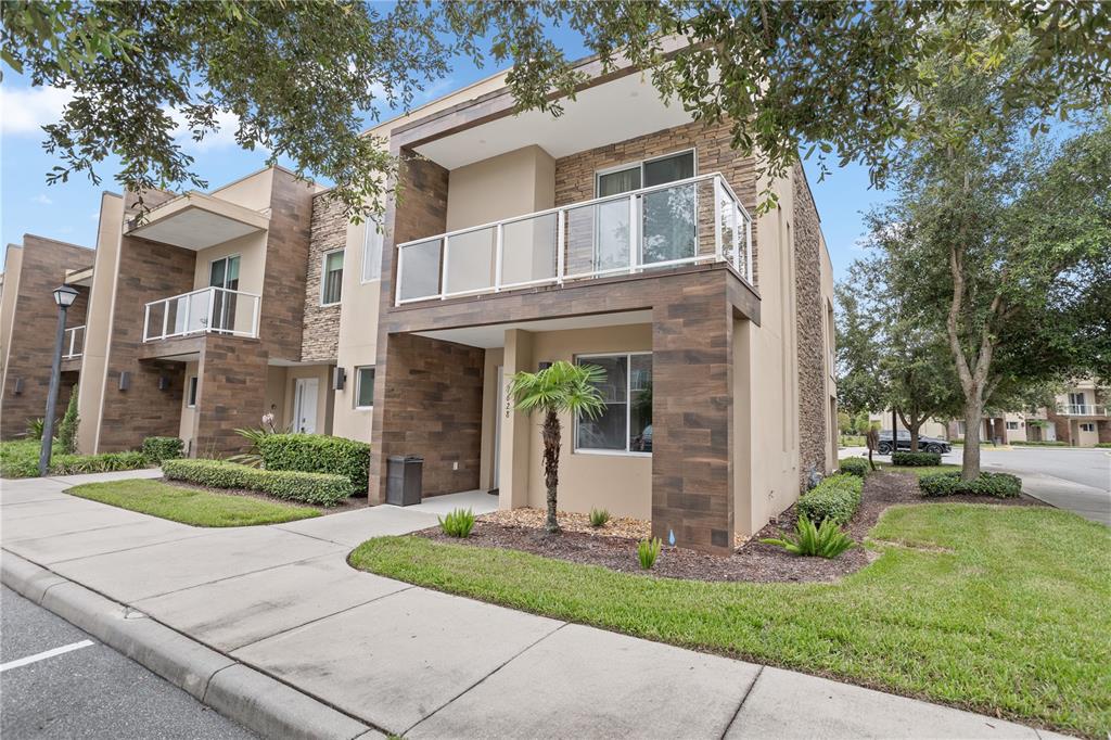 A two-story townhouse exterior features a balcony with glass railings and wood-look tile siding — 7628 RECIFE DRIVE, KISSIMMEE, FL