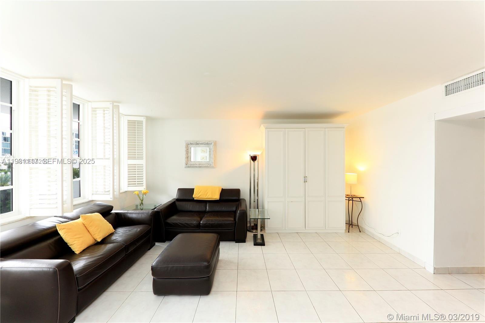 A living room features white tile floors, dark leather furniture, and white plantation shutters — 100 Lincoln Rd # 509, Miami Beach FL 33139, MIAMI BEACH, FL