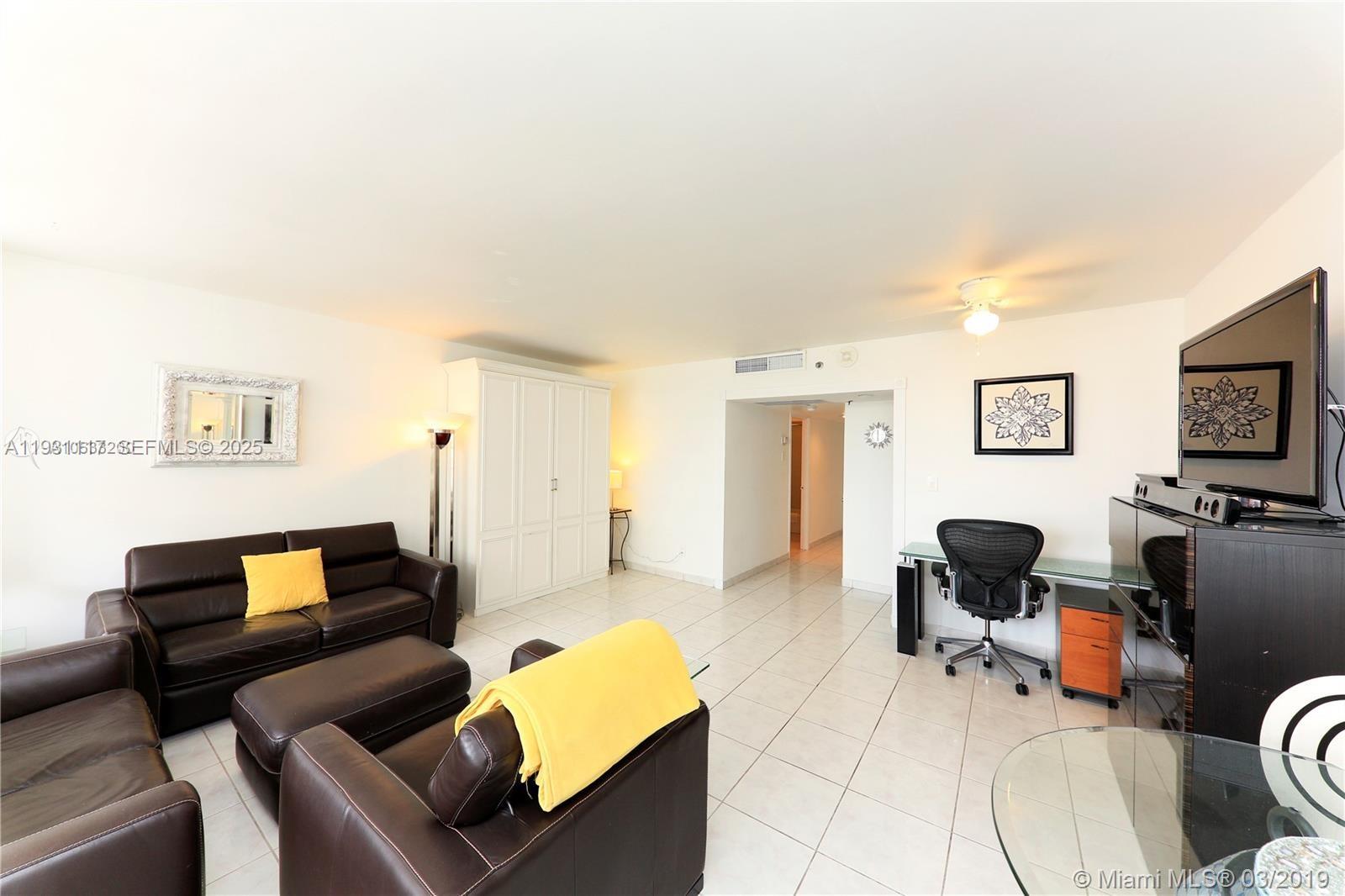 A living room features white tile floors, dark leather furniture, and a desk area — 100 Lincoln Rd # 509, Miami Beach FL 33139, MIAMI BEACH, FL