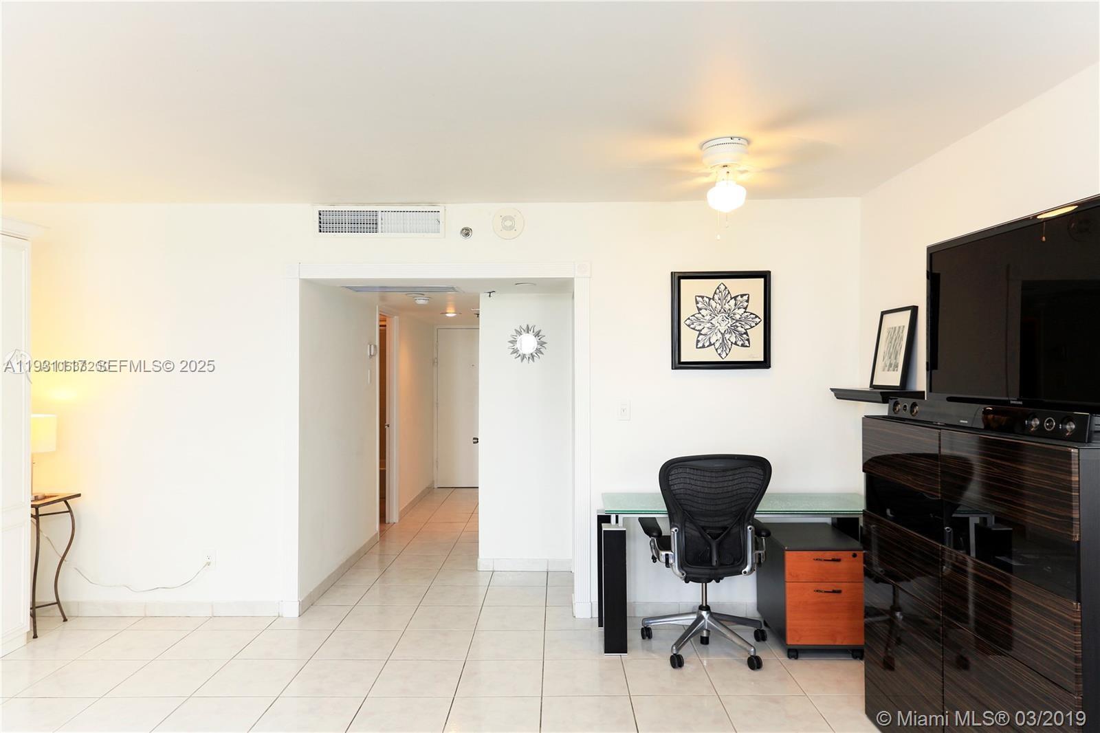 A room with white walls, tile flooring, a desk, an office chair, and a hallway — 100 Lincoln Rd # 509, Miami Beach FL 33139, MIAMI BEACH, FL