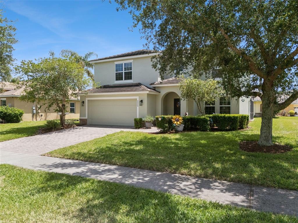 A two-story house with a beige stucco exterior, a two-car garage, and a paved driveway — 9026 PAOLOS PLACE, KISSIMMEE, FL