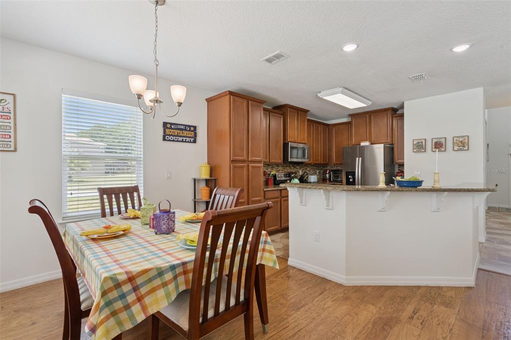A dining area with a plaid tablecloth sits adjacent to a kitchen with wood cabinets — 9026 PAOLOS PLACE, KISSIMMEE, FL