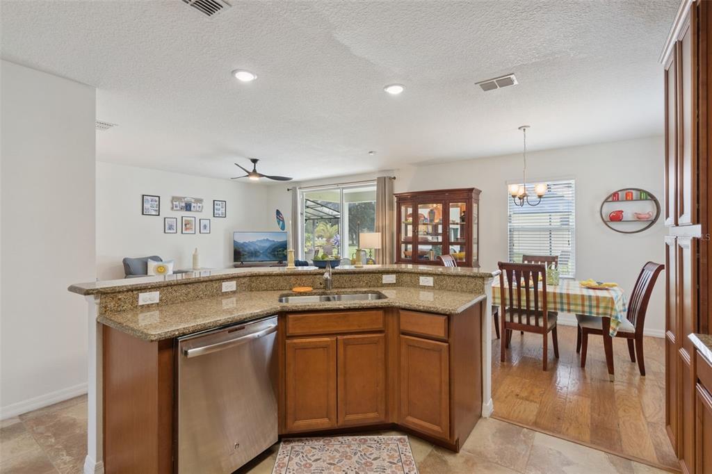 A kitchen with granite countertops and stainless steel appliances overlooks a dining area and living room — 9026 PAOLOS PLACE, KISSIMMEE, FL