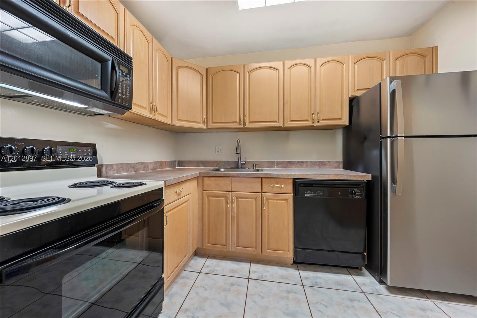 A kitchen features light wood cabinets, black appliances, a stainless steel refrigerator, and tiled floors — 7829 Miller Dr # B205, Miami FL 33155, MIAMI, FL