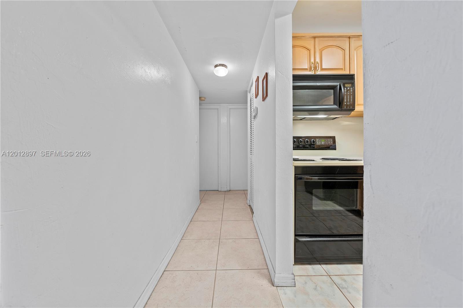 A hallway with tile flooring leads to a kitchen featuring light wood cabinets and appliances — 7829 Miller Dr # B205, Miami FL 33155, MIAMI, FL