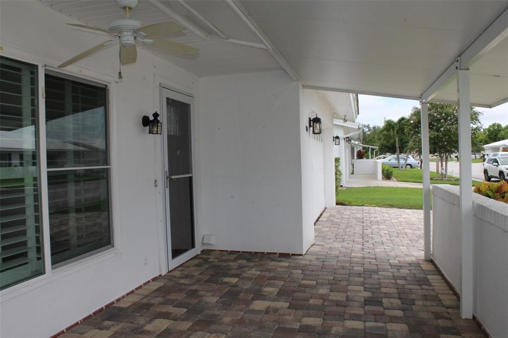 A covered patio features paver flooring, a ceiling fan, and exterior wall-mounted light fixtures — 9045 40TH STREET N, PINELLAS PARK, FL