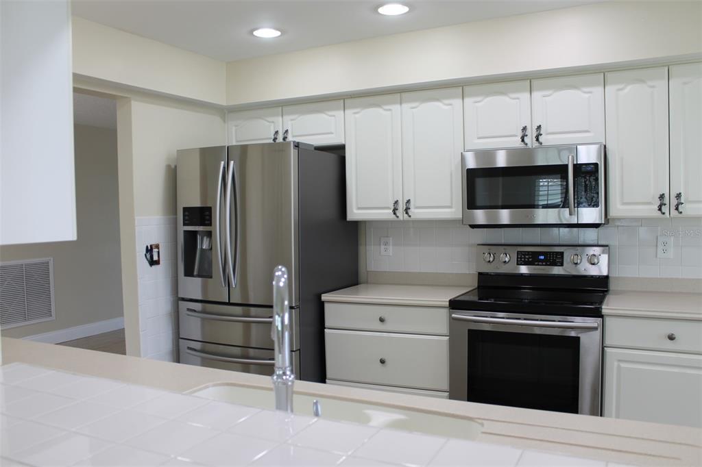 A kitchen with white cabinets, stainless steel appliances, and a tiled countertop and backsplash — 9045 40TH STREET N, PINELLAS PARK, FL