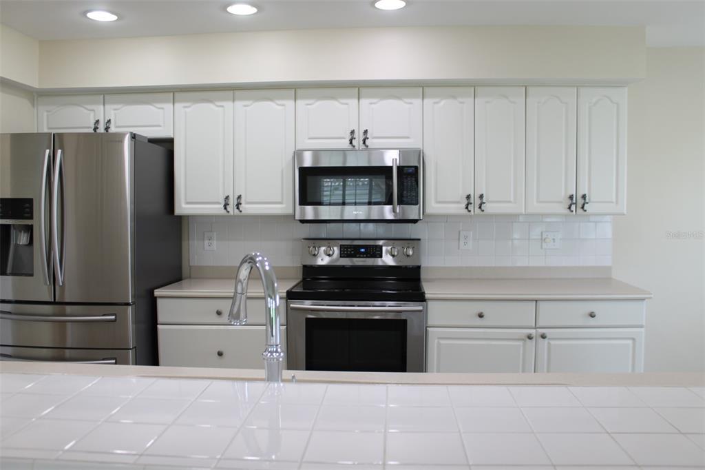 A kitchen features white cabinets, stainless steel appliances, and a tiled countertop and backsplash — 9045 40TH STREET N, PINELLAS PARK, FL