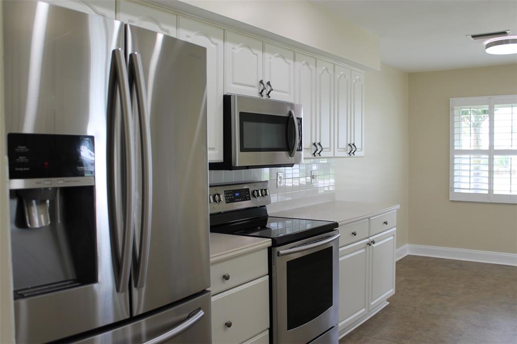 A kitchen features stainless steel appliances, white cabinetry, and a window with plantation shutters — 9045 40TH STREET N, PINELLAS PARK, FL