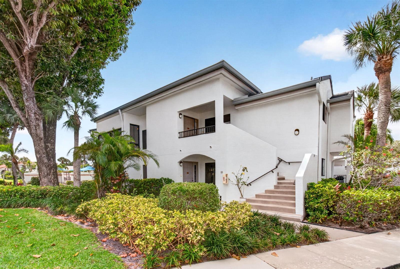 A two-story white stucco building with an exterior staircase and lush tropical landscaping — 7485 Glendevon Lane # 1105, Delray Beach FL 33446, DELRAY BEACH, FL