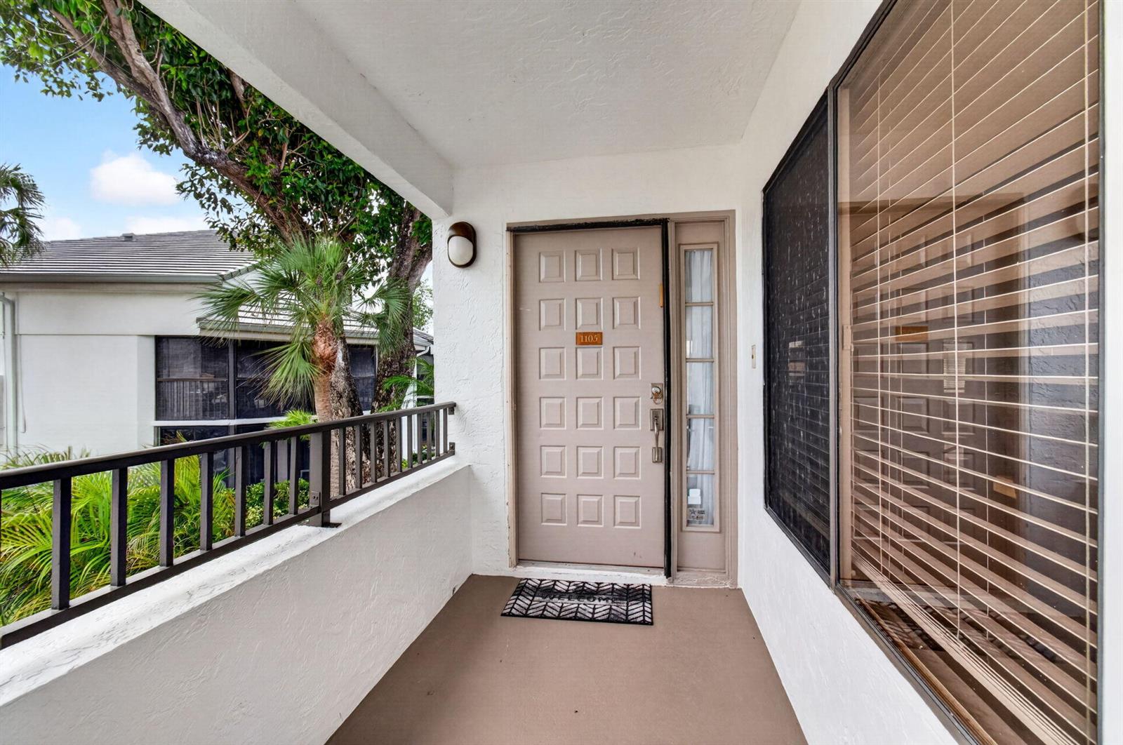 A covered entryway features a tan paneled door, a side window, and a metal railing — 7485 Glendevon Lane # 1105, Delray Beach FL 33446, DELRAY BEACH, FL
